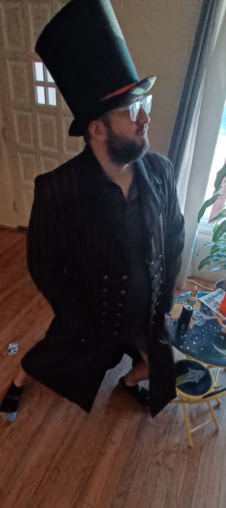 The creator of Oolong Water, in a tall top hat, pinstripe coat, and glasses, standing in socks with a theatrical Wonkler pose.